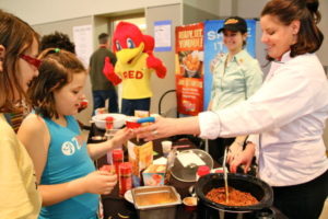Red Robin Chef Rachael Minor and other Red Robin associates serving young Athletes for Christ participants, Red Robin Mascot Red standing next to their booth